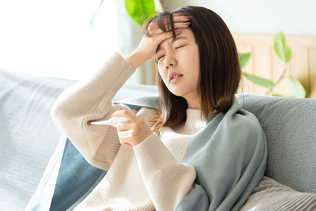 体温計で熱を計り額に手をあてる女性